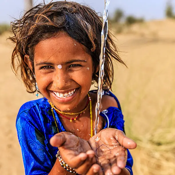 a littile girl in thar desert seems to be happy after seeing water 